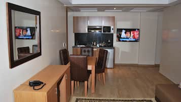 A compact living space with a dining area, kitchenette, and a TV mounted on the wall.