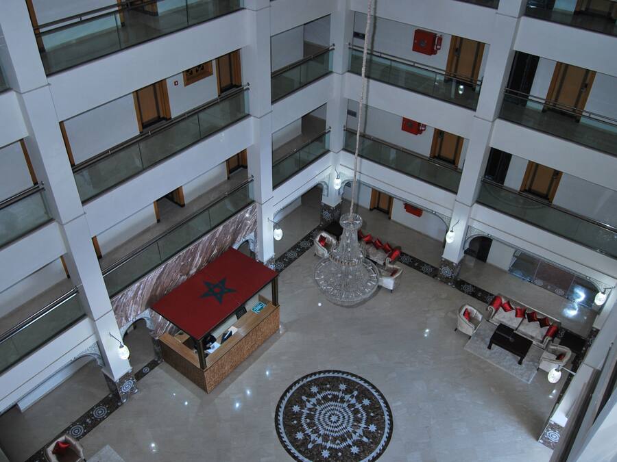Un atrio de varios niveles con una zona de estar central, un pequeño quiosco con techo rojo y un diseño decorativo en el suelo.