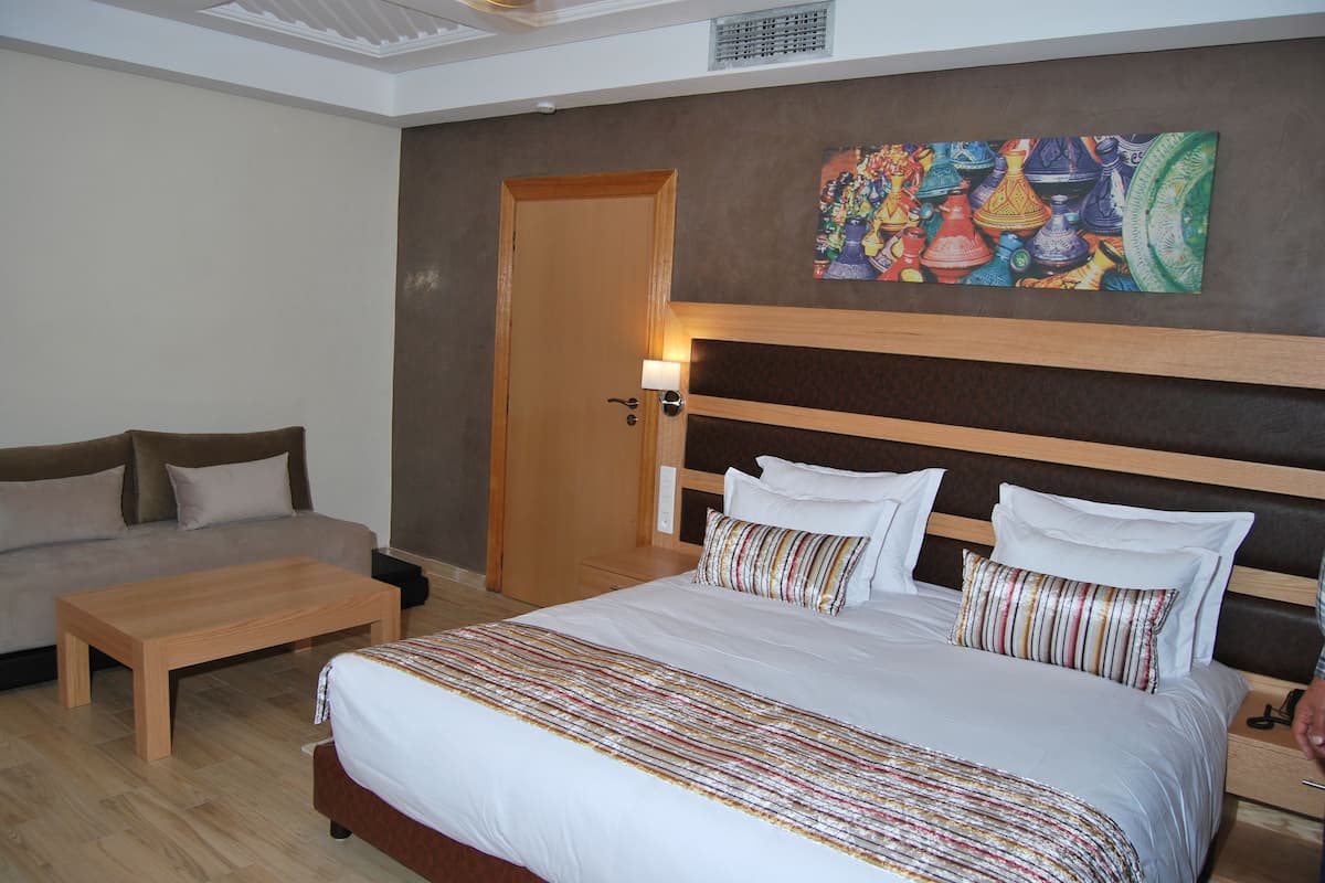 A hotel room with a bed, a sofa, a wooden coffee table, and a painting on the wall.