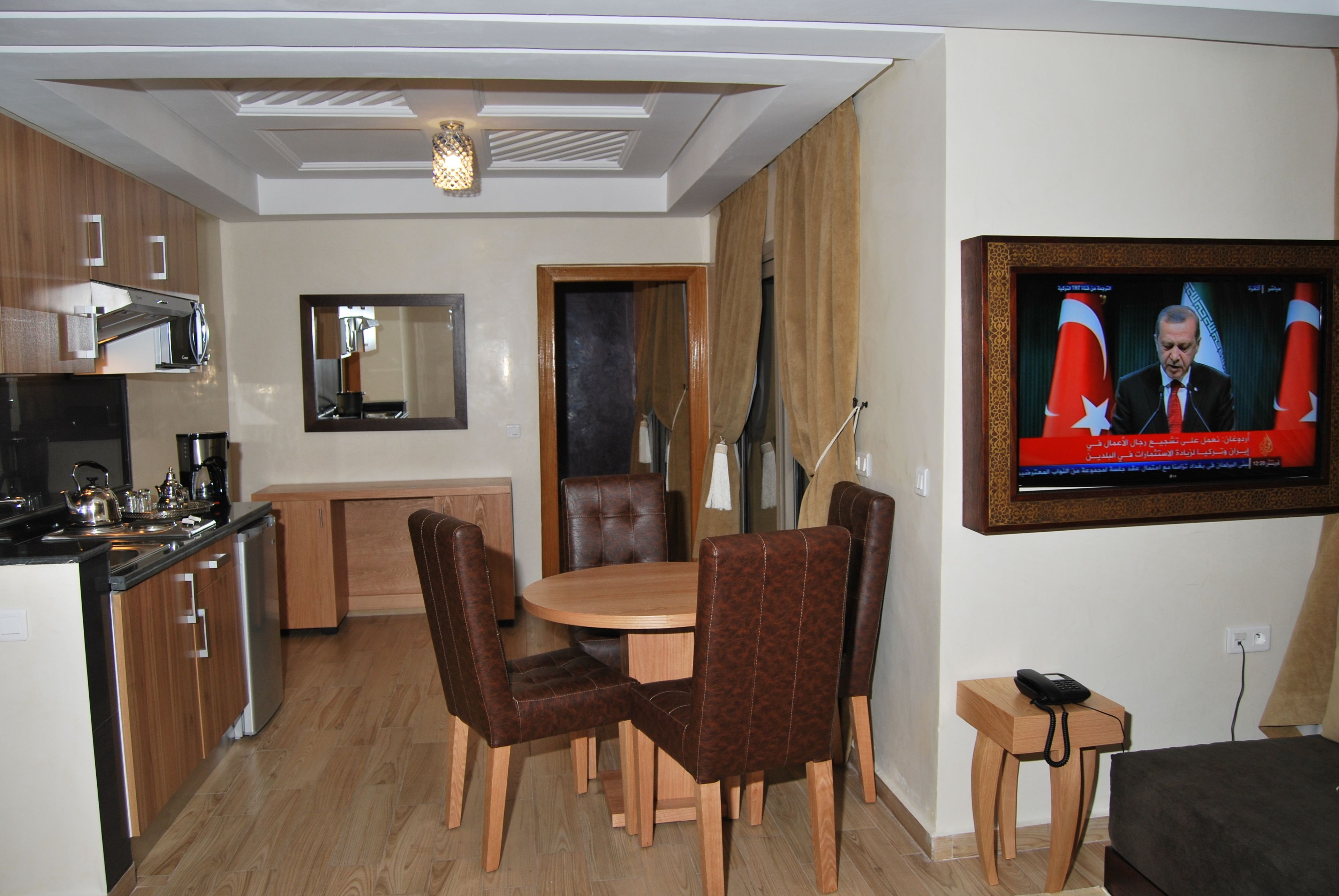 Habitació d'hotel moderna amb zona de dinar, cuina i televisió que mostra un informatiu.