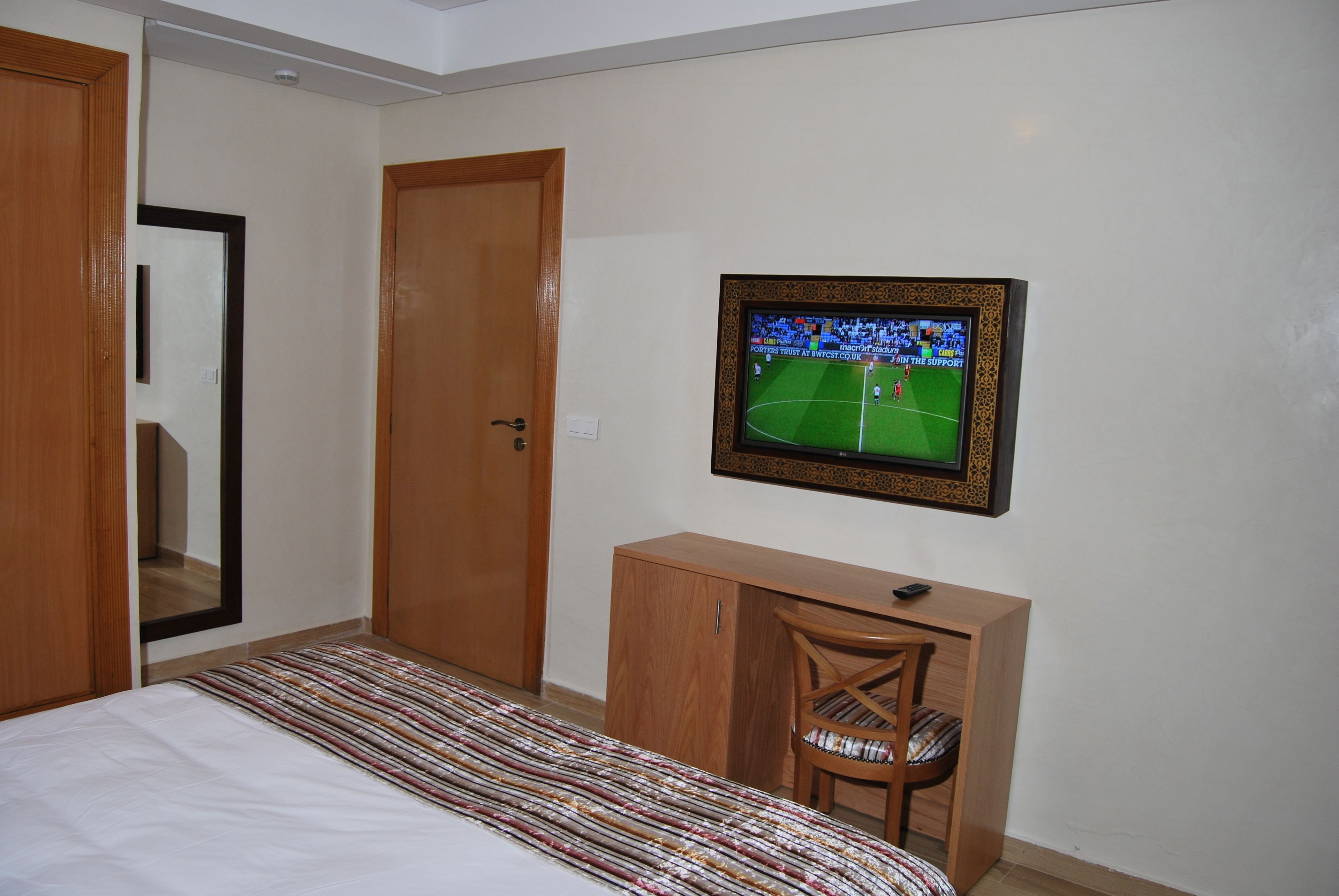 Une chambre à coucher comprenant un lit, un bureau, une chaise et un téléviseur diffusant un événement sportif.