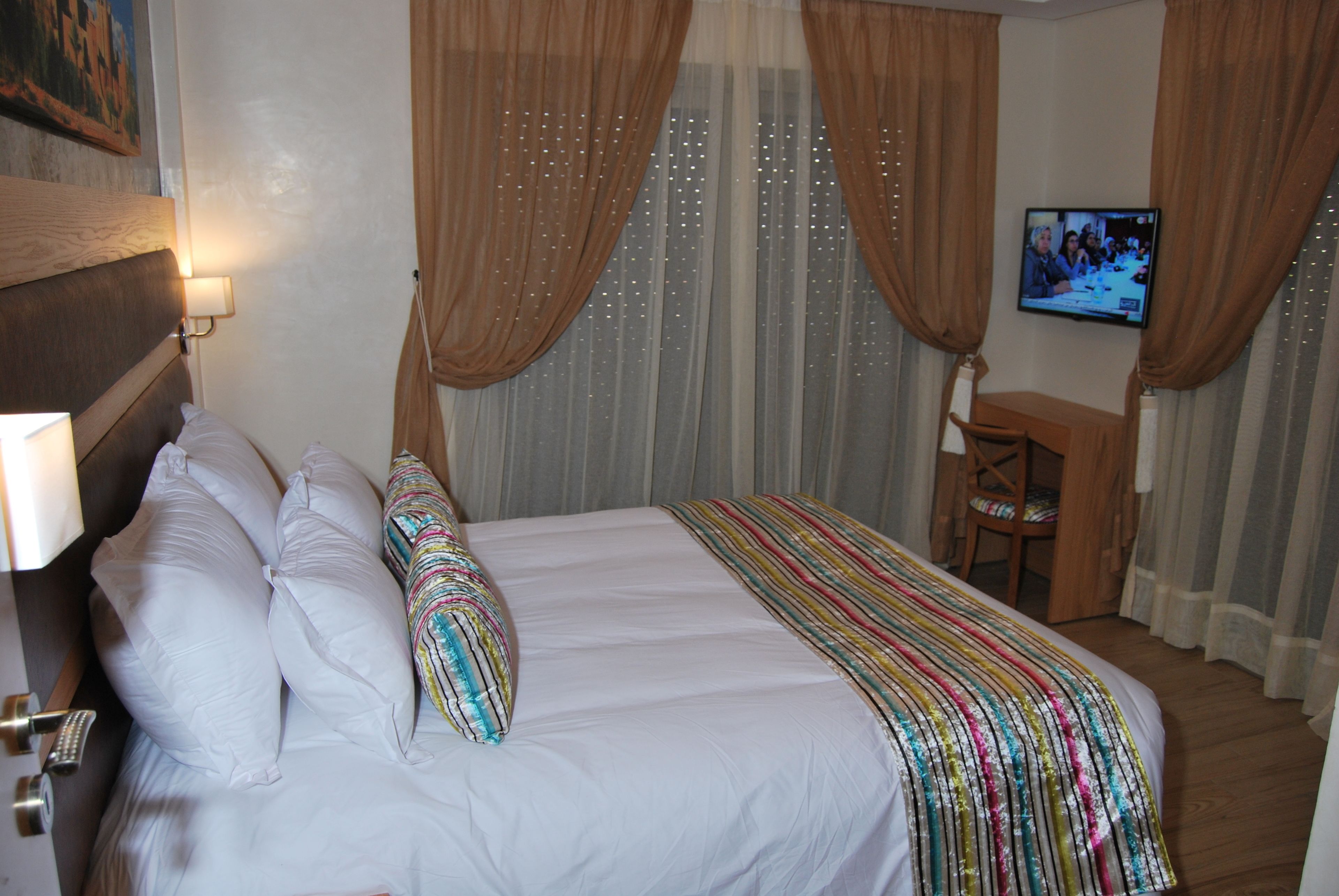 A hotel room with a bed, curtains, a television, and a desk.