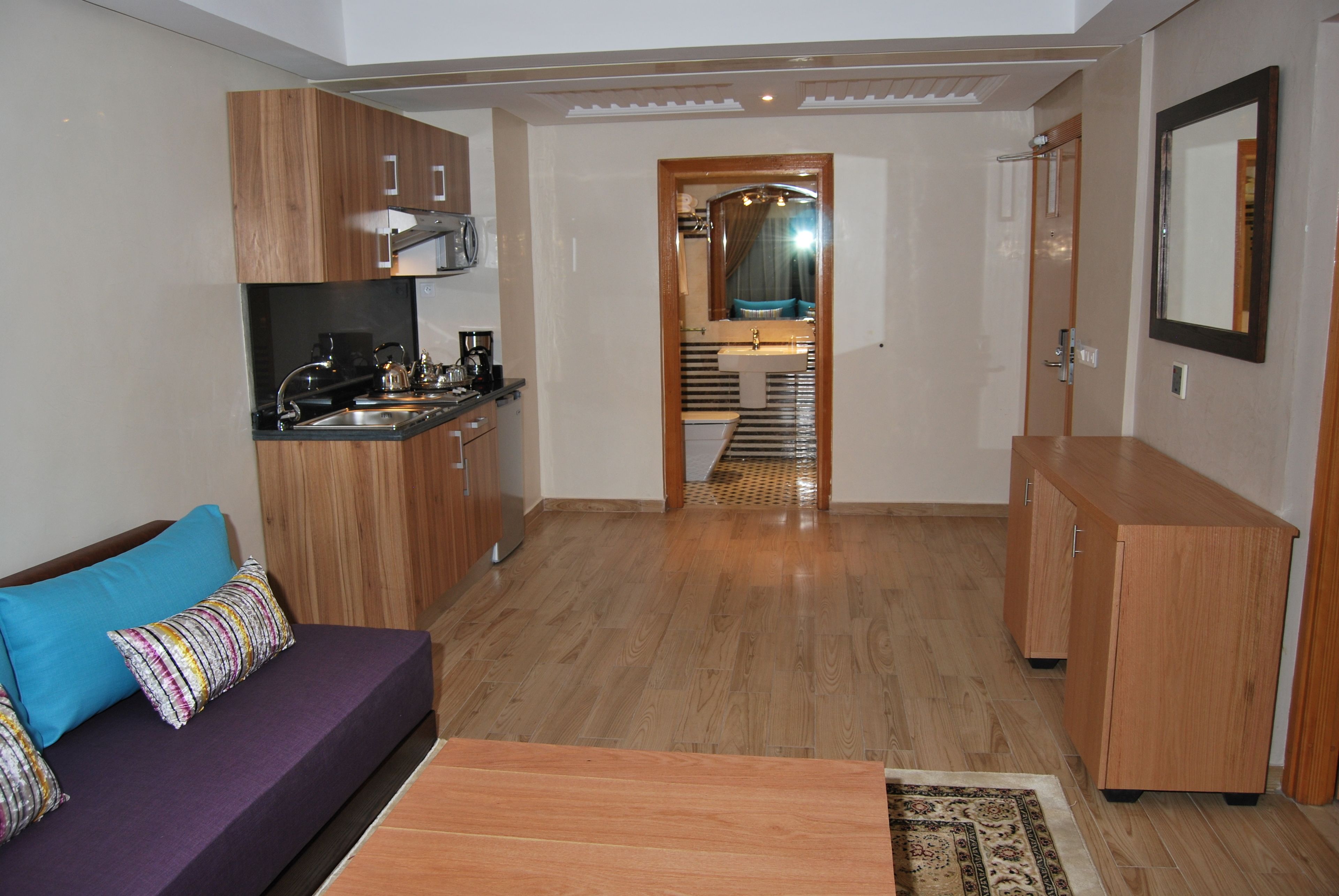 A modern living room with a sofa, a coffee table, wooden cabinets, and a kitchen area with a sink and appliances.