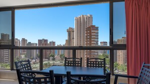 A balcony with a table and chairs, a red curtain, and a city view through large windows. - APARTAMENTOS GEMELOS 20 - BENINTER (Benidorm)