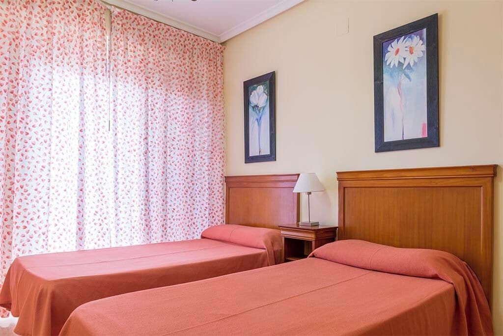 Een hotelkamer met twee bedden, een houten hoofdbord, een nachtkastje met een lamp en bloemen gordijnen.