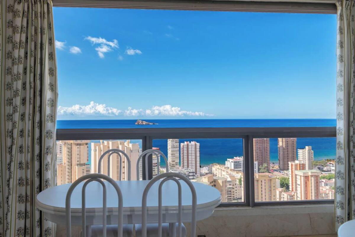 Ein Balkon mit Tisch und Stühlen mit Blick auf Stadt und Meer.