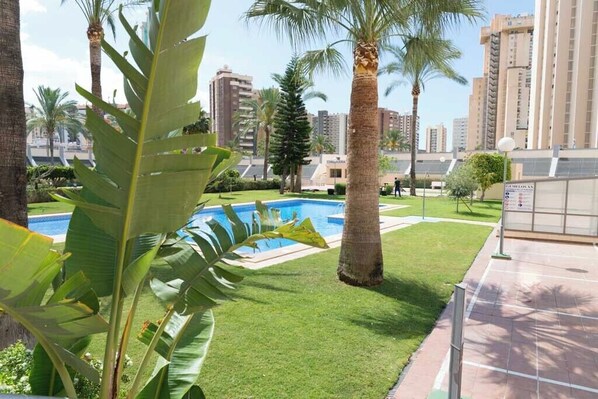 Zona residenziale con piscina, palme e edifici moderni sullo sfondo.