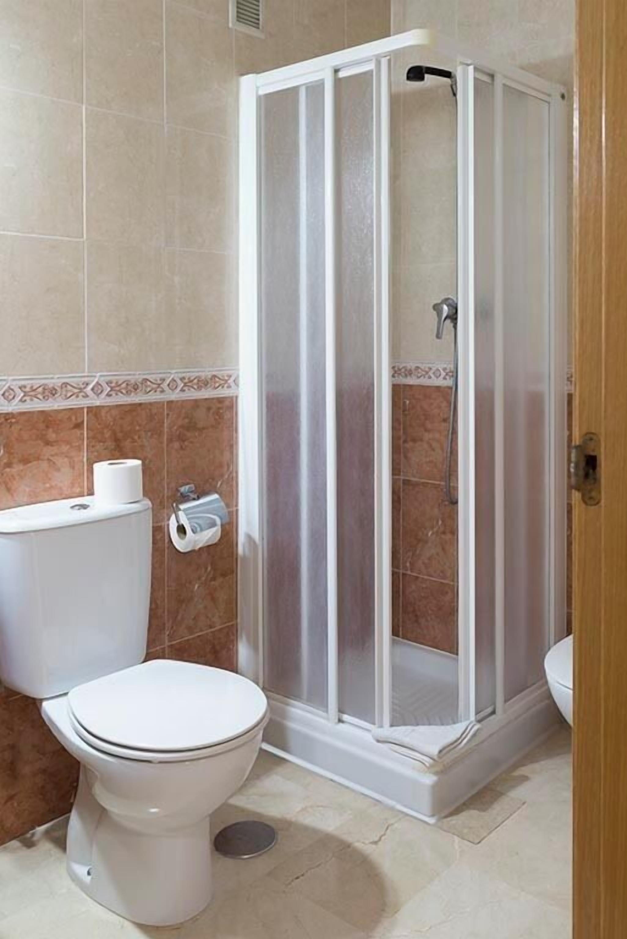 A bathroom with a toilet, a shower enclosure, and a toilet paper holder.