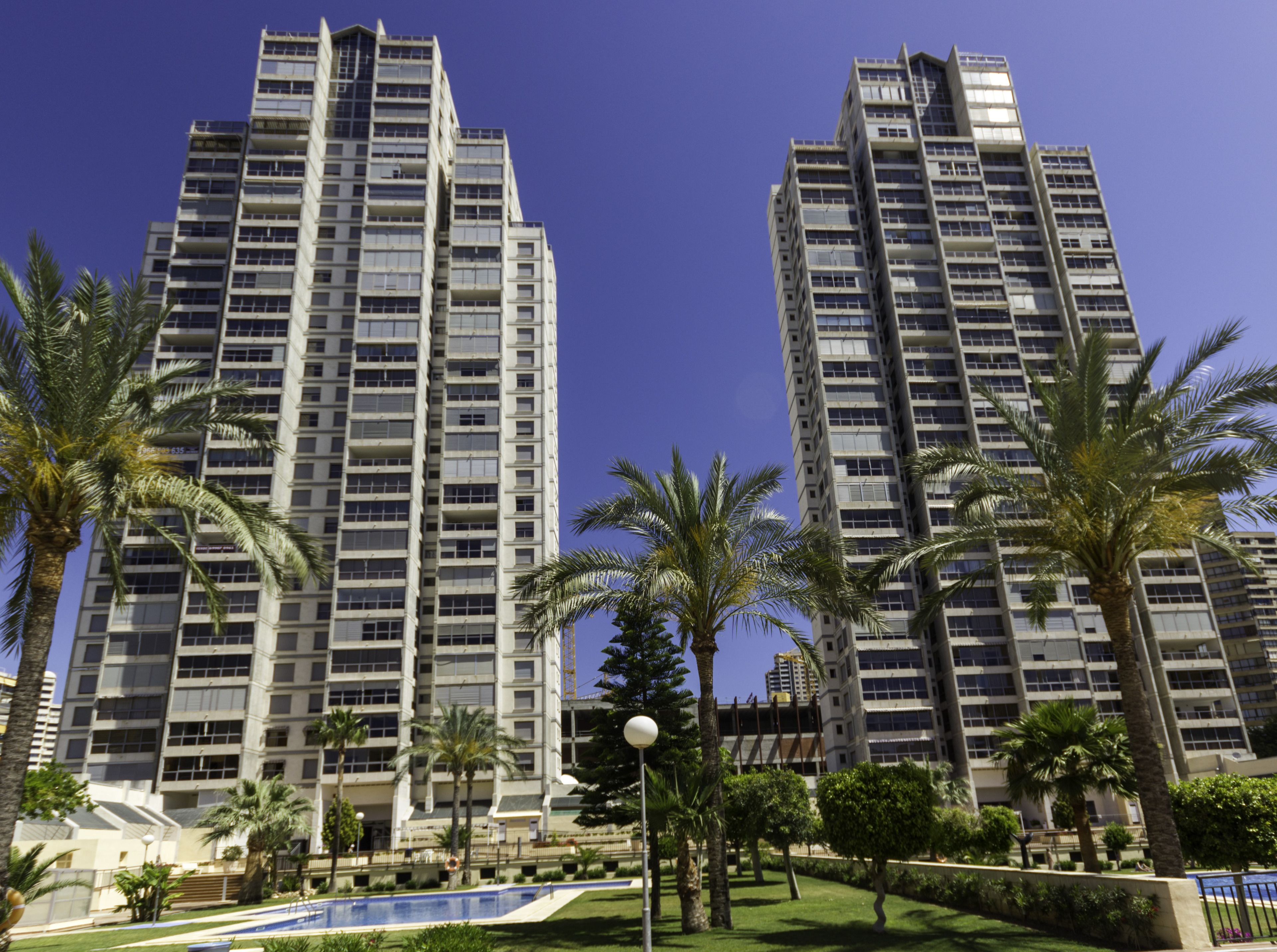 Two high-rise buildings with a swimming pool and palm trees in the foreground.