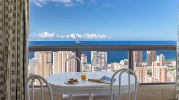 A balcony with a table, chairs, and a view of the city and ocean. - APARTAMENTOS GEMELOS 20 - BENINTER (Benidorm)