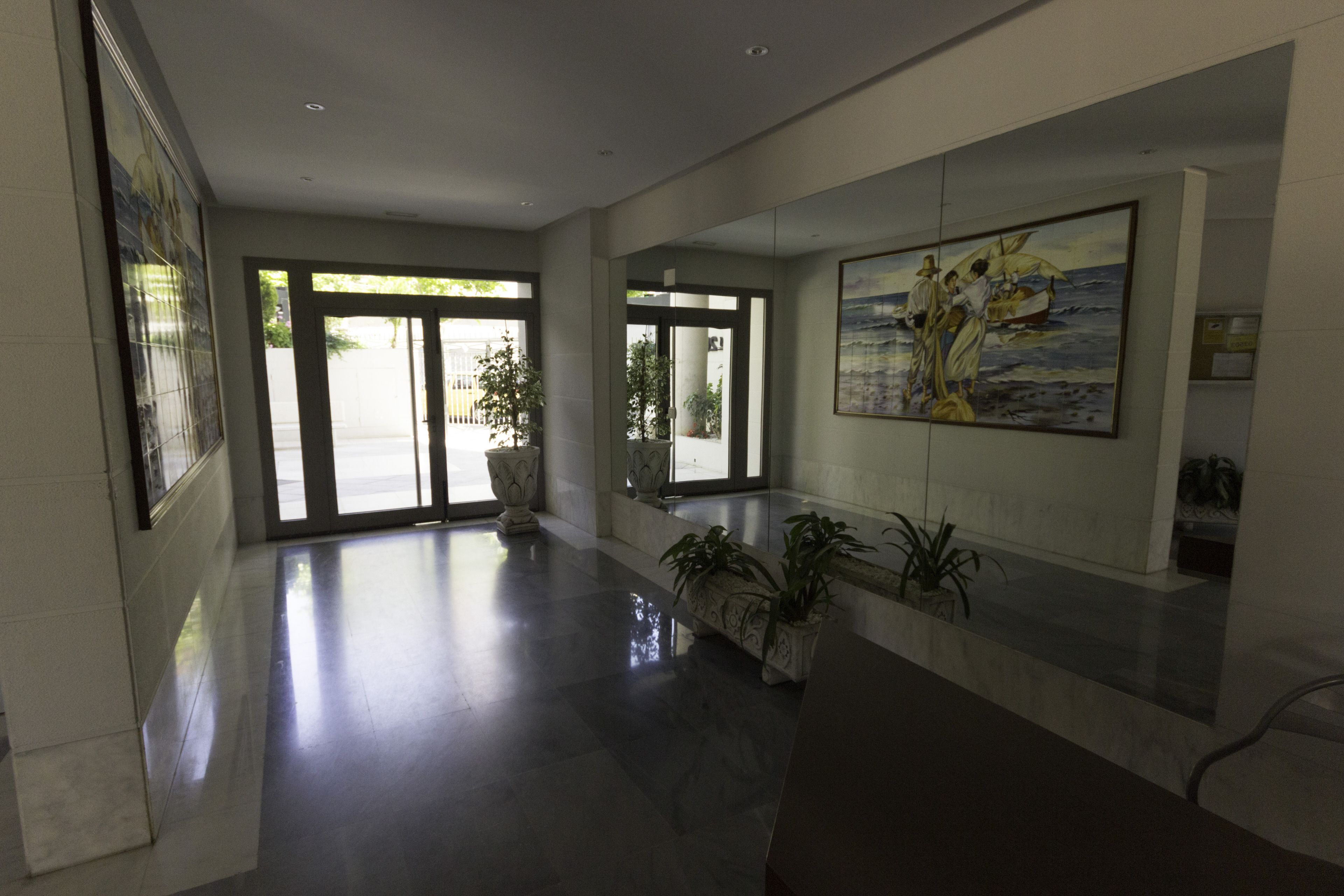 A spacious lobby with a polished floor, large windows, and potted plants.