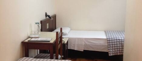 A hotel room with two beds, a desk, a chair, a television, and two framed pictures on the wall.