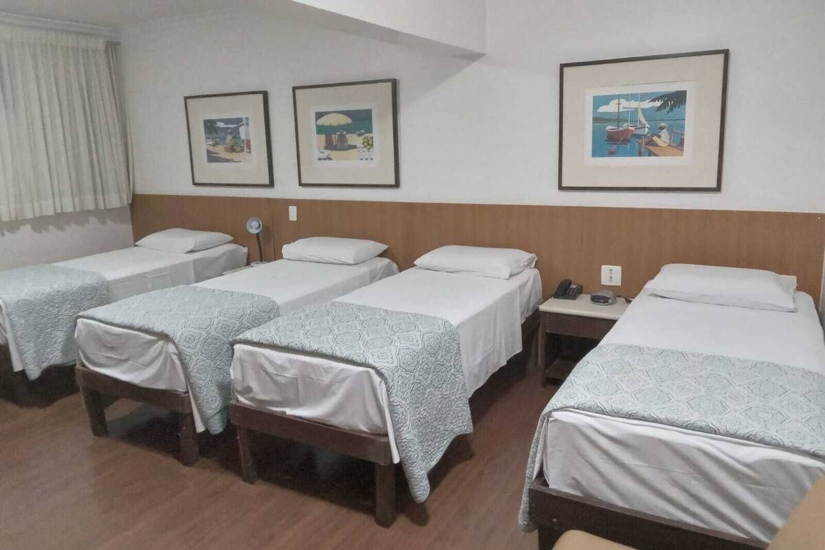 A hotel room with four single beds, a small bedside table with a phone, and three framed pictures on the wall.