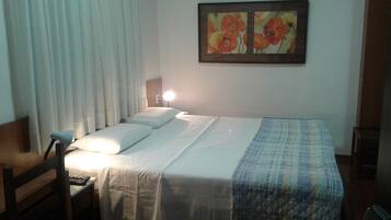 Quarto de hotel com cama, uma cadeira, mesa de cabeceira e um quadro na parede.