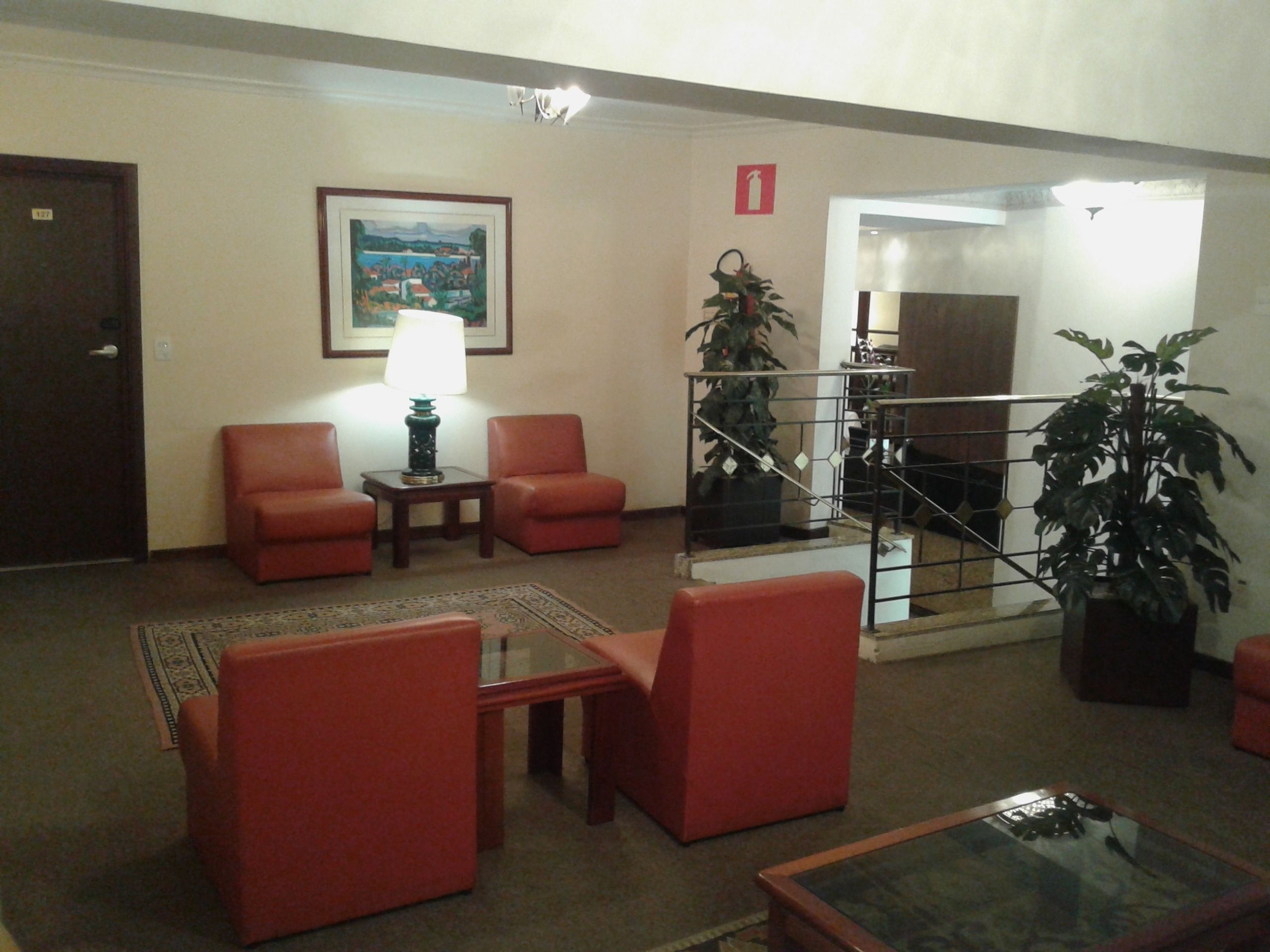Un vestíbulo con sillones rojos, una mesa con lámpara, un cuadro enmarco y una escalera con barandilla.