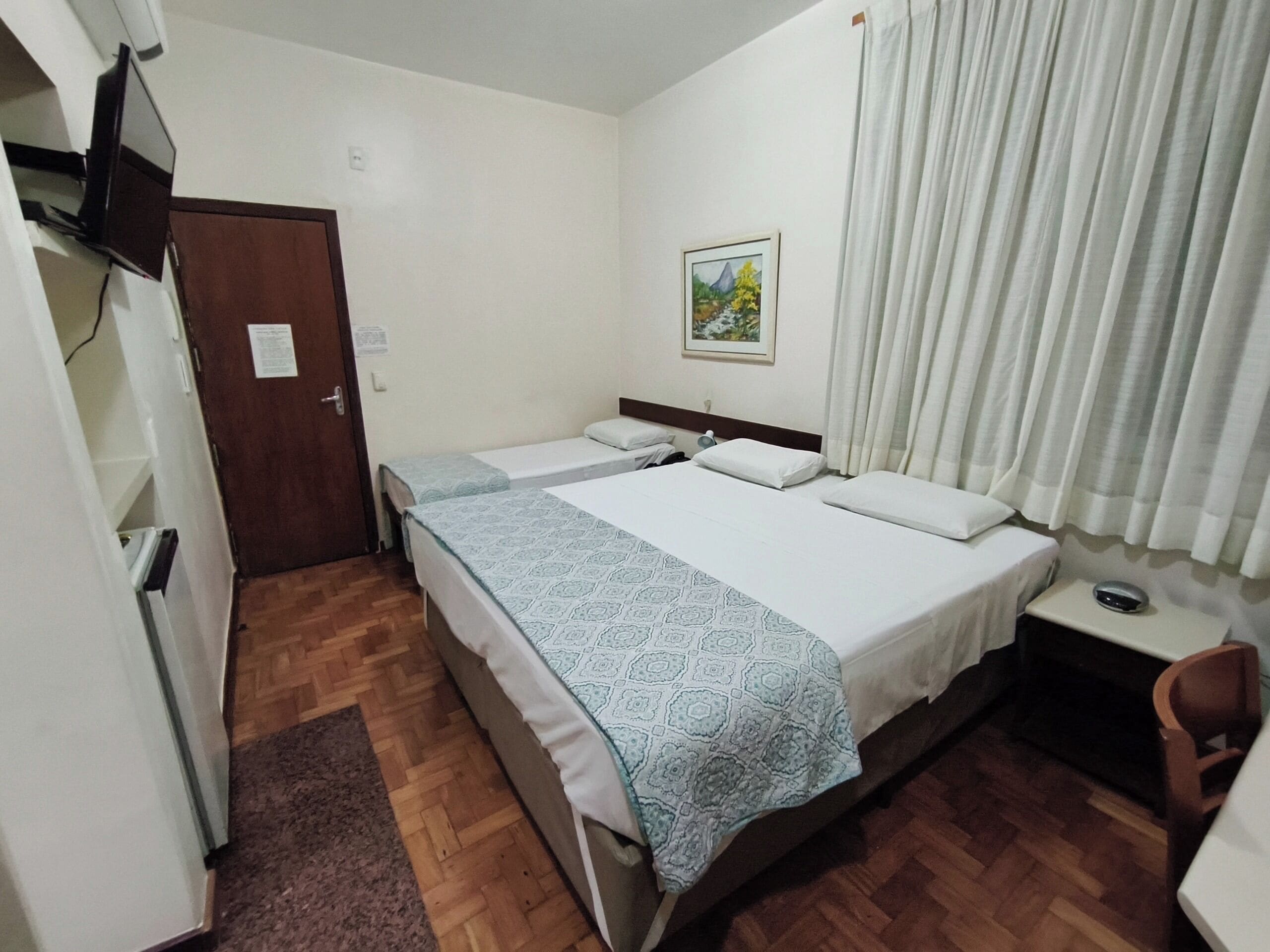A hotel room with two beds, a desk, a chair, a television, and a painting on the wall.