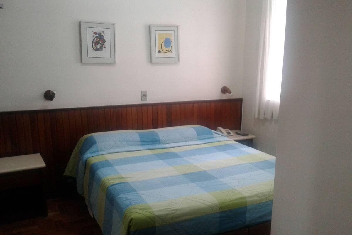 A hotel room with a bed, a bedside table, a telephone, and two framed pictures on the wall.