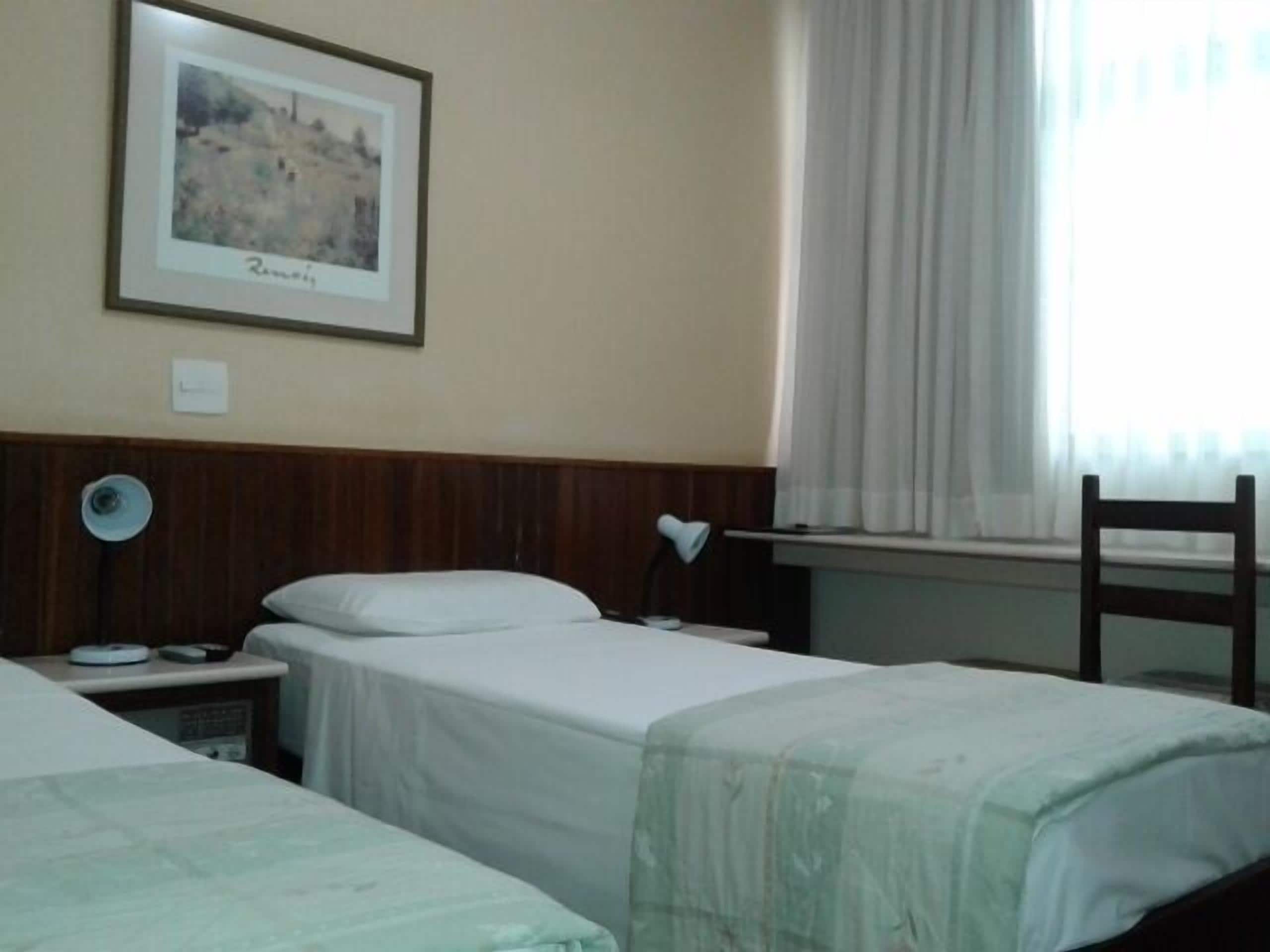 A hotel room with two beds, a nightstand, a desk, a chair, and a window with curtains.