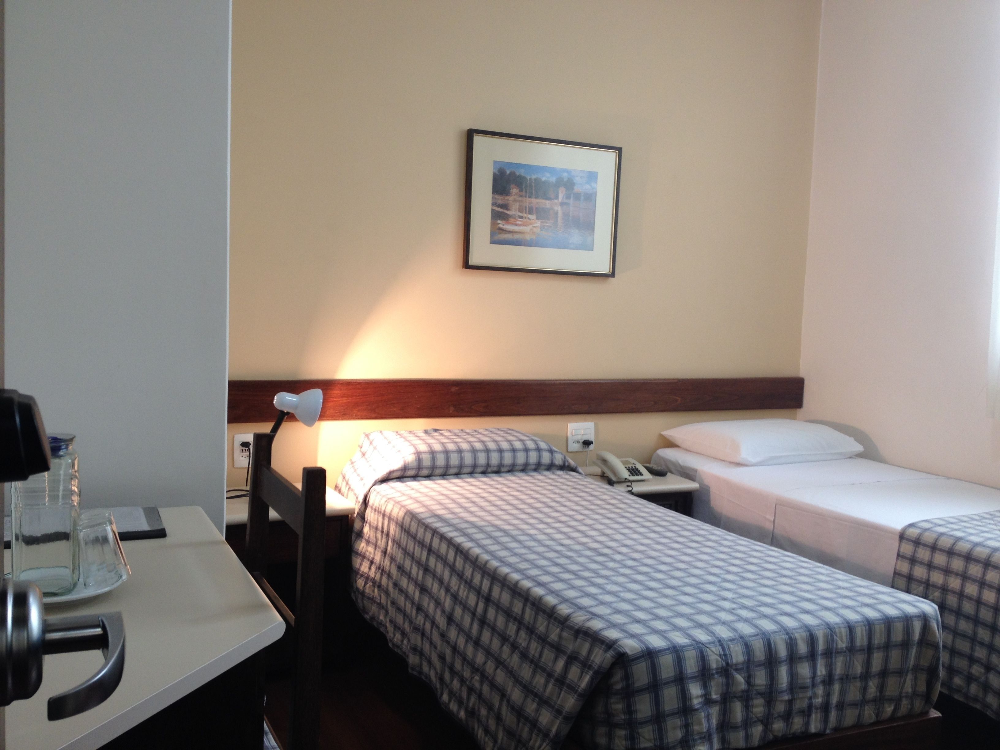 Hotellihuoneessa on kaksi sänkyä, työpöytä, lamppu ja seinällä oleva kehystetty kuva.