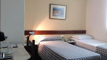 A hotel room with two beds, a desk, a lamp, and a framed picture on the wall.
