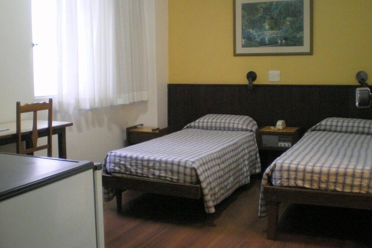 A room with two beds, a desk, a chair, and a window with curtains.
