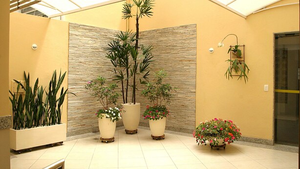 A spacious indoor area with a high ceiling and a skylight, featuring several potted plants and a wall with a textured pattern. - Hotel São Bento (Belo Horizonte)