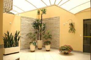 A spacious indoor area with a high ceiling and a skylight, featuring several potted plants and a wall with a textured pattern. - Hotel São Bento (Belo Horizonte)