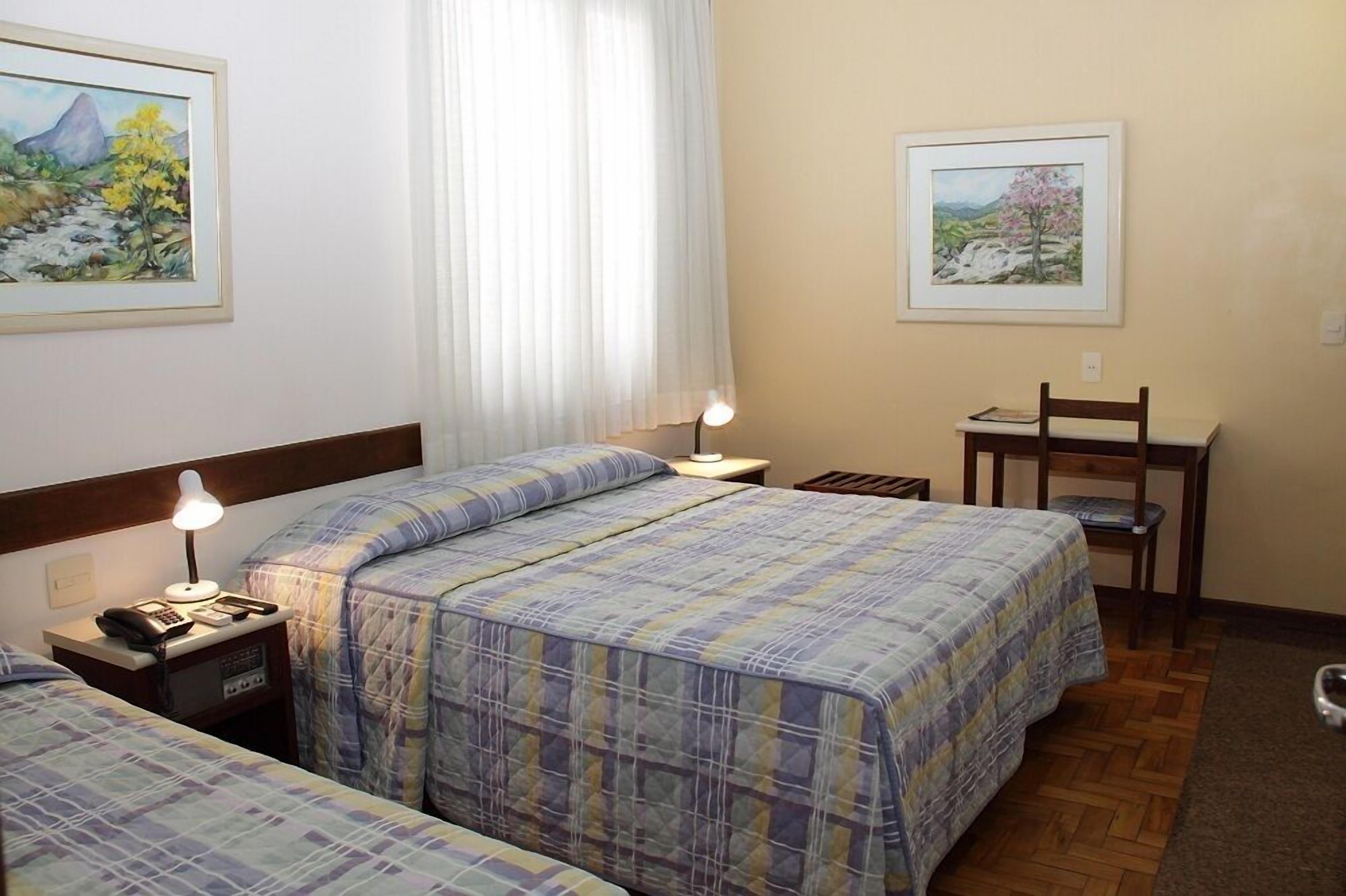 Una habitación de hotel con dos camas, un escritorio, una silla y una lámpara.