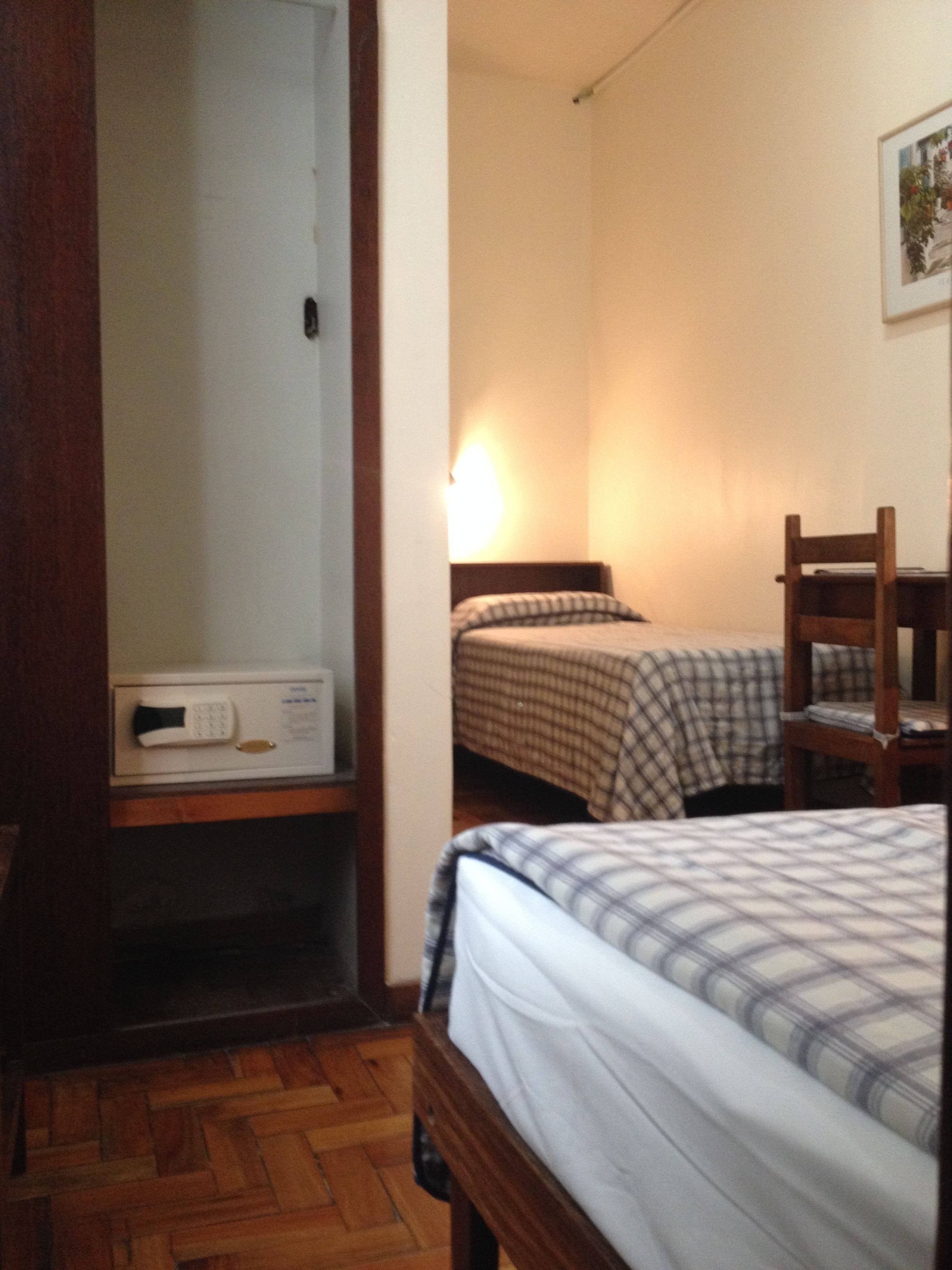 A bedroom with a bed, a chair, a bedside table, and a wall-mounted lamp.