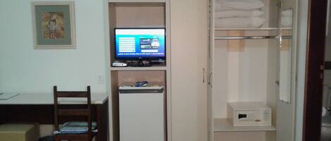 Habitación compacta con cama, escritorio con computadora, refrigerador pequeño y armario con espacio para colgar.