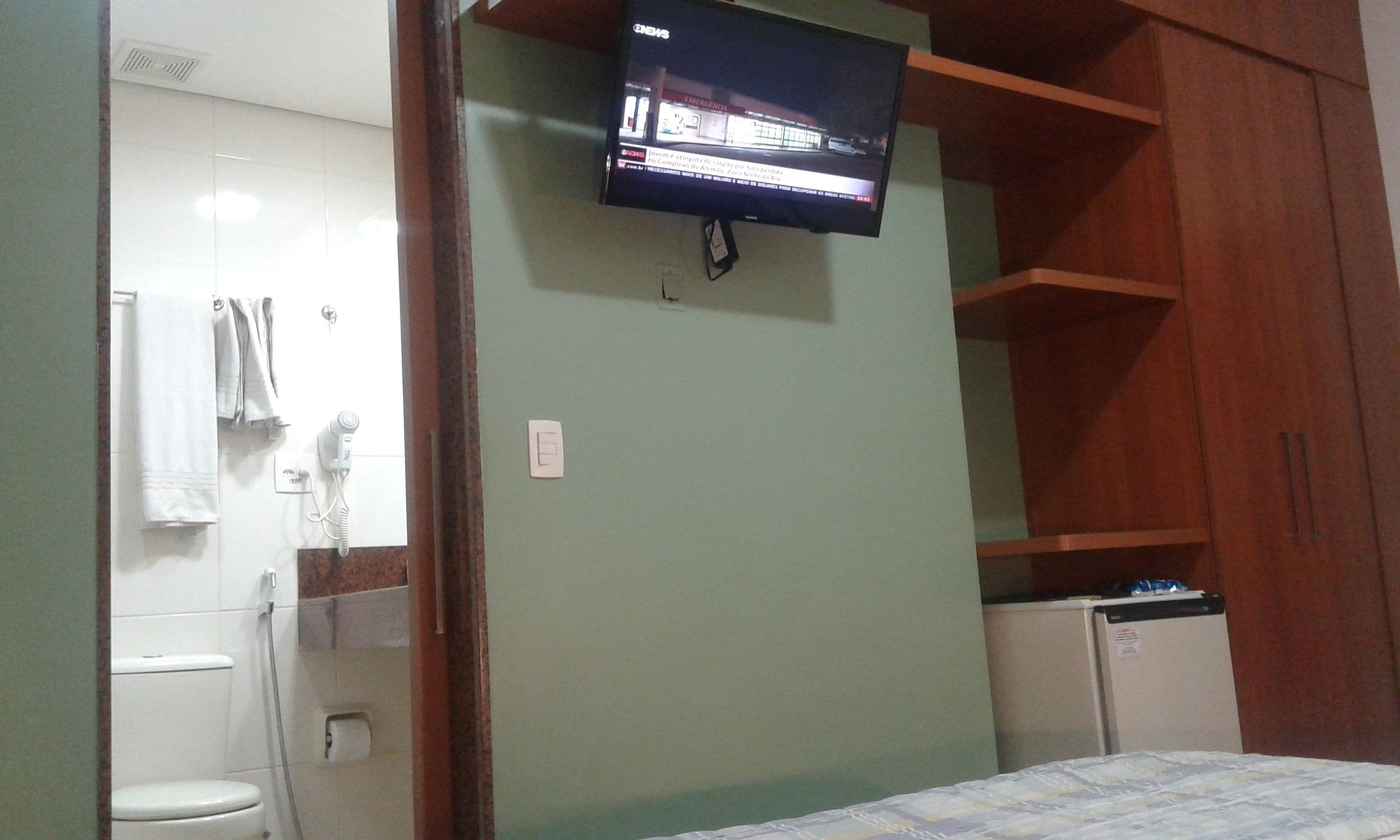Un baño con inodoro, secador de pelo y televisor montado en la pared.