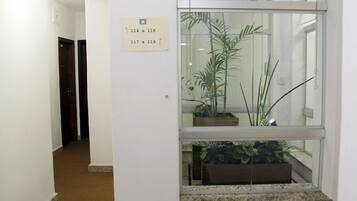 A hallway with a sign indicating room numbers 114 to 119. There are potted plants in a window display.