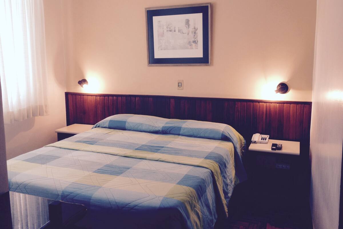 A hotel room with a bed, bedside tables, a framed picture on the wall, and a telephone on the nightstand.