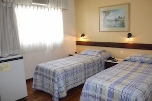 Hotellihuone, jossa on kaksi sänkyä, työpöytä, jääkaappi ja taulu seinällä.