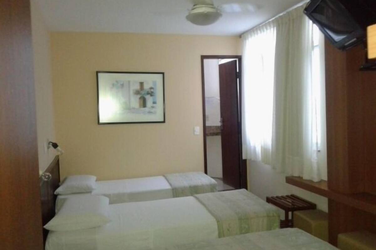 A room with two beds, a ceiling fan, a framed picture on the wall, and a door leading to another room.