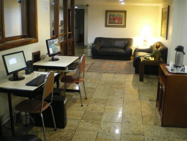 A room with a desk, computer, and a couch. There is a lamp on a side table and a painting on the wall.