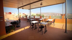 A terrace with tables and chairs, potted plants, and a view of a cityscape.