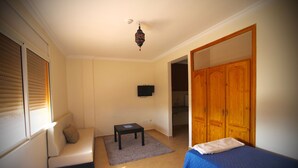 A room with two beds, a sofa, a television, and a wooden wardrobe.