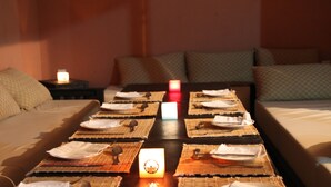 A neatly arranged dining table with placemats, cutlery, and candles, set in a room with a bed and pillows.