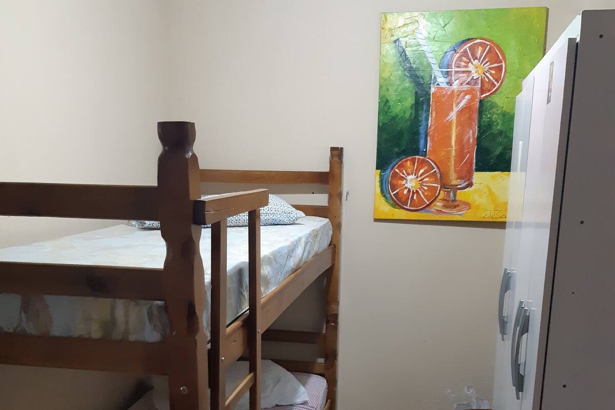 Une chambre avec un lit superposé, un tableau représentant des agrumes accroché au mur, une petite table et un placard.