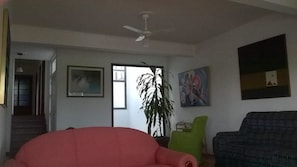 A living room with a ceiling fan, a staircase, a large window, and a green chair.