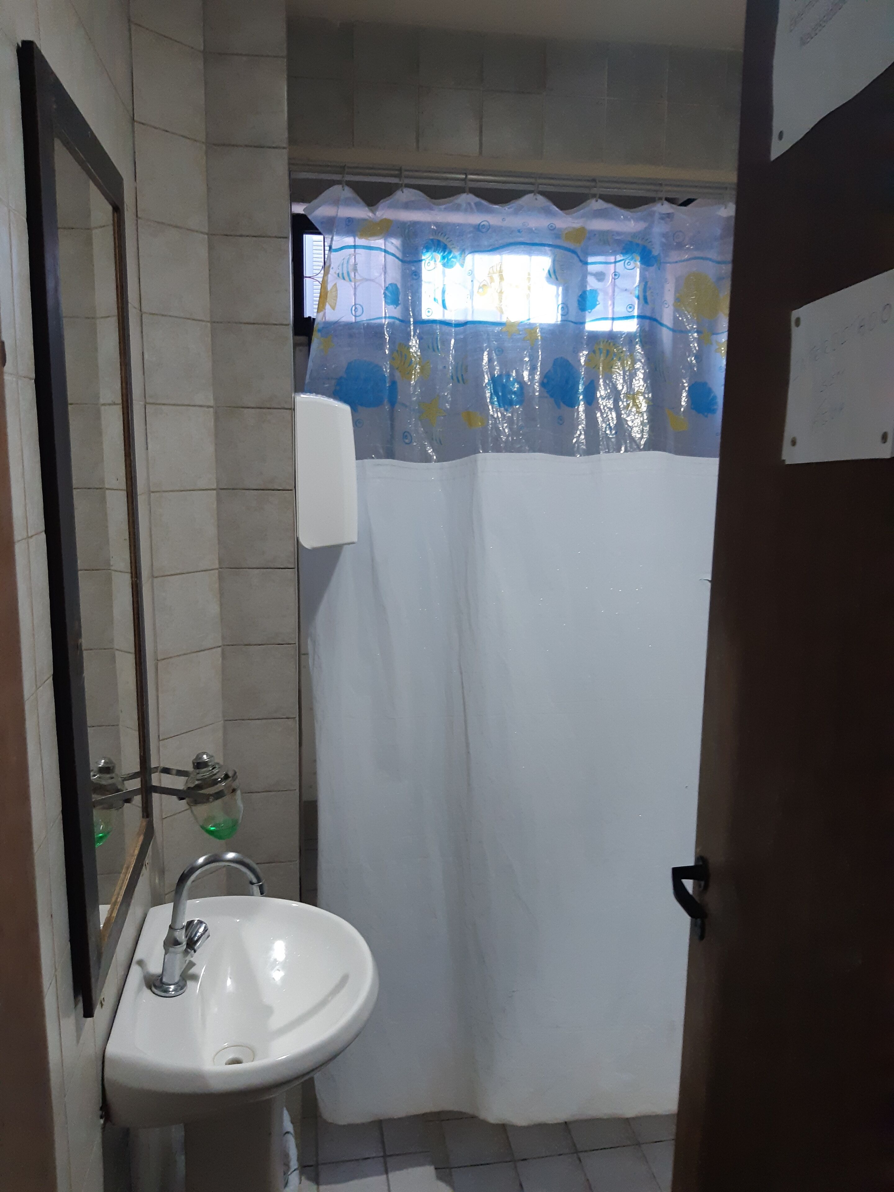 Un baño con un lavamanos blanco, un espejo y una cortina de ducha estampada con motivos florales.