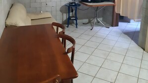 A compact living space with a tiled floor, a wooden dining table, a sofa, a television on a stand, and a wall-mounted fan.