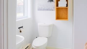 Een badkamer met toilet, wastafel, vloertegels met patroon, een raam en een houten plank met handdoeken.