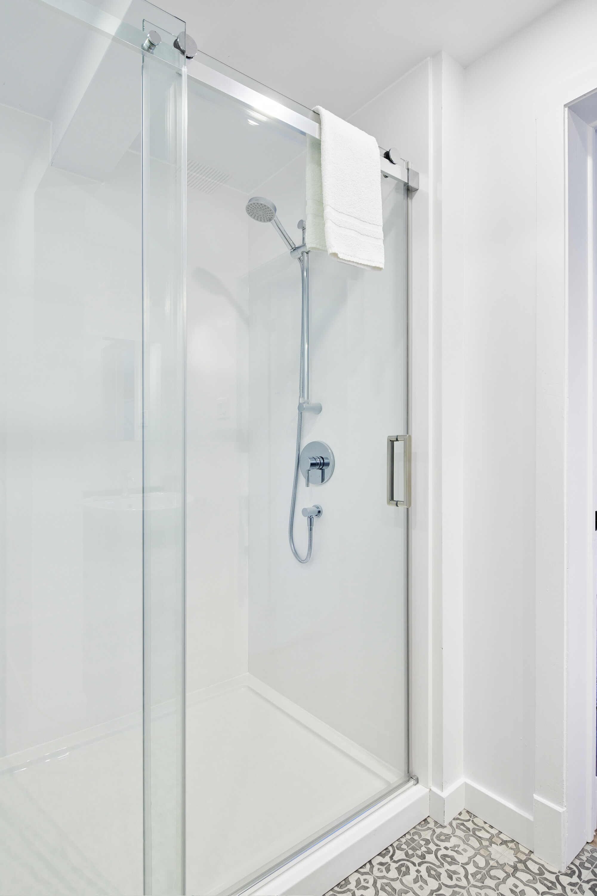 A glass-enclosed shower with a handheld showerhead and a wall-mounted faucet.