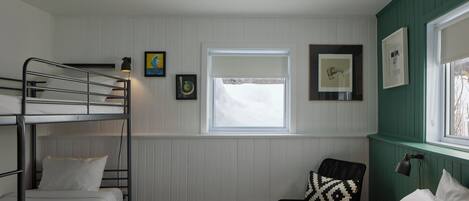 A dormitory room with bunk beds, a window, and framed artwork on the walls.