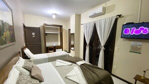 Habitación de hotel con dos camas, un televisor, aire acondicionado, un armario y una pequeña mesa con un florero.