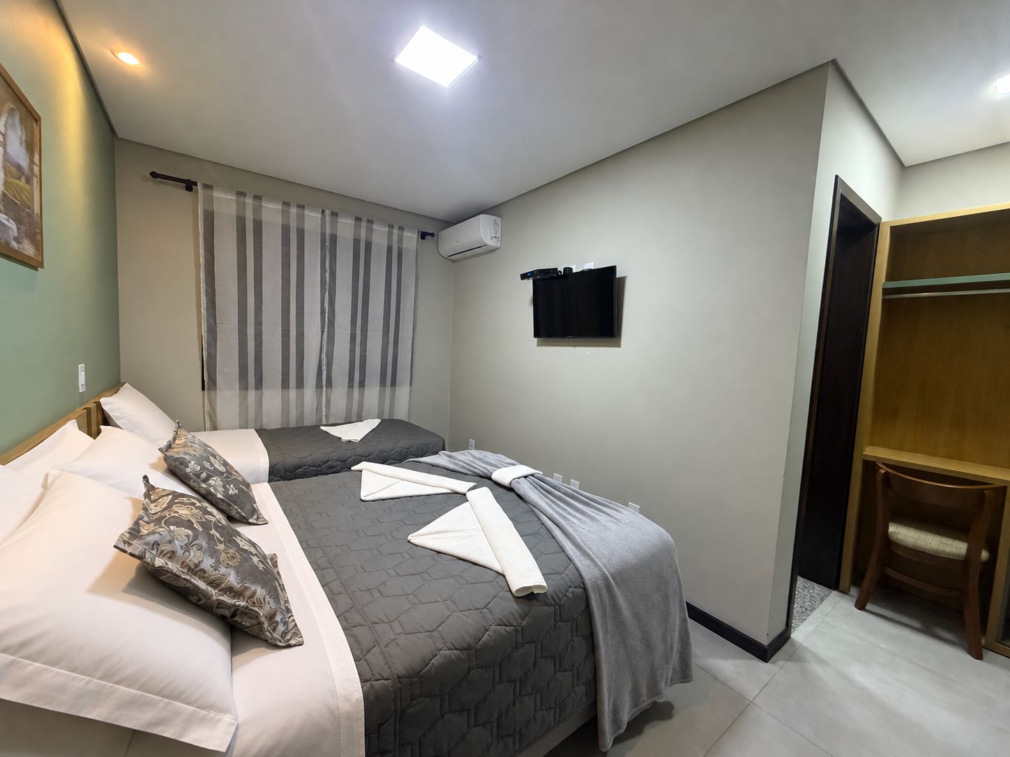 Une chambre d’hôtel avec deux lits, une télévision, un appareil de climatisation, une chaise en bois et une armoire.