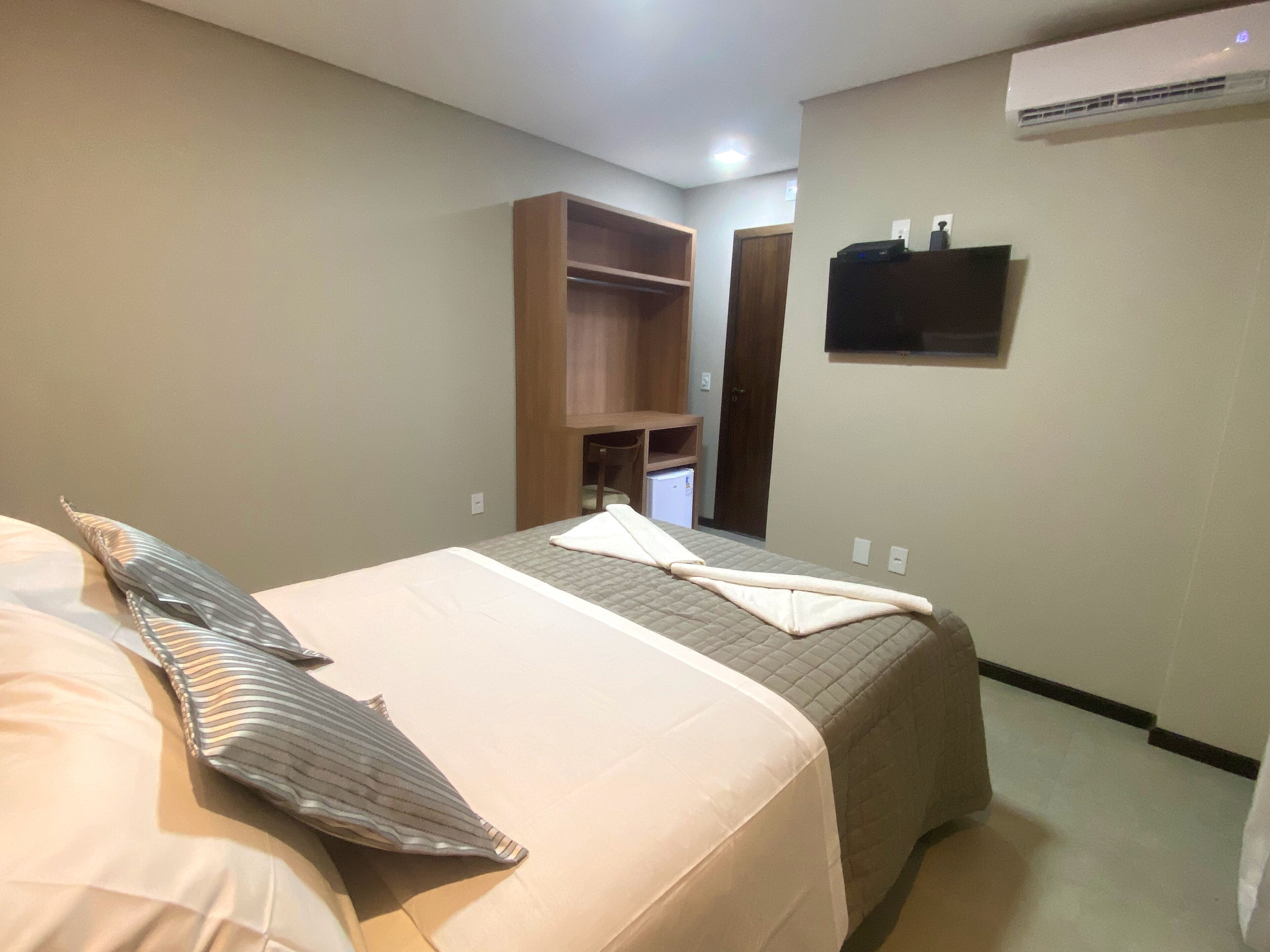 Habitación de hotel con cama, armario, un refrigerador pequeño y unidad de aire acondicionado.