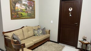 Una sala de estar con un sofá color beige, cojines estampados, una silla de madera, un tapete, una puerta y un cuadro en la pared.